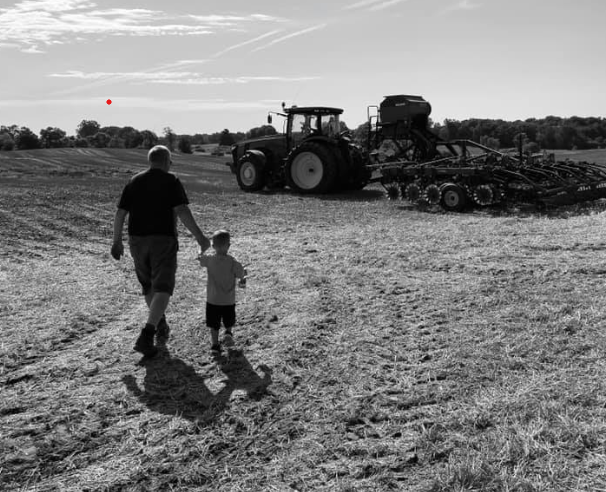 A black and white photo of Doug Westendorp walking away from the camera while holding hands with a young family member